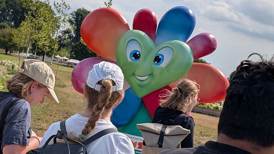 Personen in einem grünen Freiraum. Im Hintergrund eine bunte Skulptur.