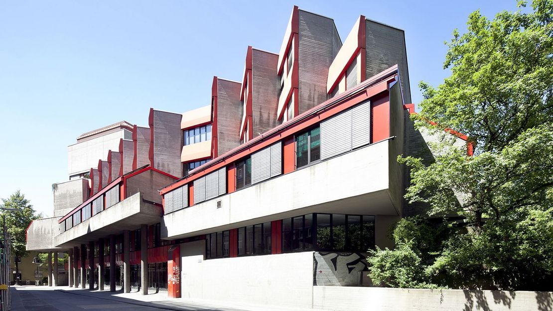Hochschule für Musik und Tank Köln Kleinteilig gegliederter Gebäudekomplex aus Beton mit roten Fassadendetails und Fensterrahmen