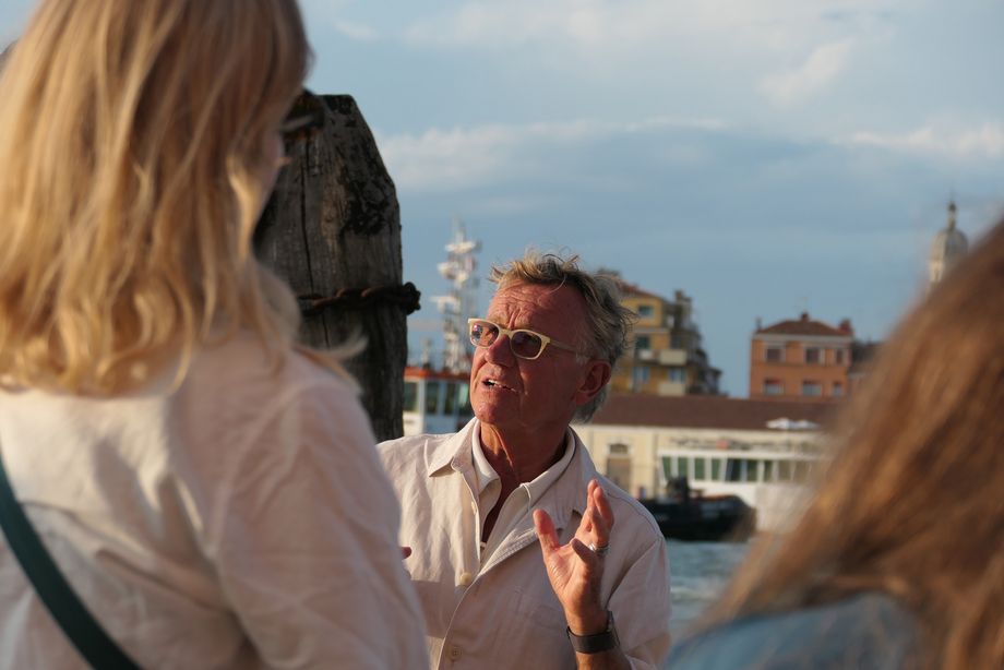 Ein Mann spricht zu einer Gruppe von Personen, der Mann gestikuliert mit den Händen. Im Hintergrund ist Wasser und eine Gebäude-Skyline zu erkennen.