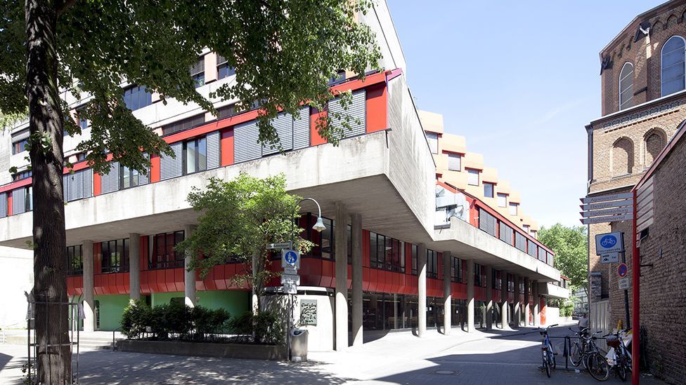 Hochschule für Musik und Tanz in Köln. Gezeigt werden zwei Gebäude im Anschnitt, im Vordergrund steht ein Baum.