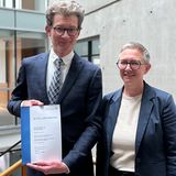 Zwei Personen stehen nebeneinander und lächeln in die Kamera.