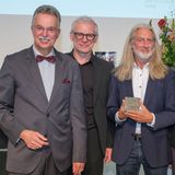 Eine Gruppe Menschen schaut und lächelt in eine Kamera. Ein Mann in der Mitte zeigt eine Medaille, u.a. mit der Aufschrift "Friedrich Halstenberg Medaille". - Foto: Detlef Podehl