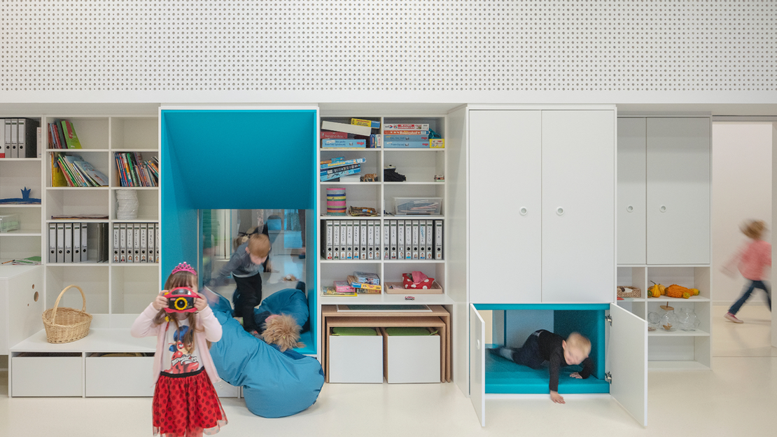 Klassenzimmer mit farblich gestalteter Regal-/Schrankwandkombination, in dem Kinder spielen
