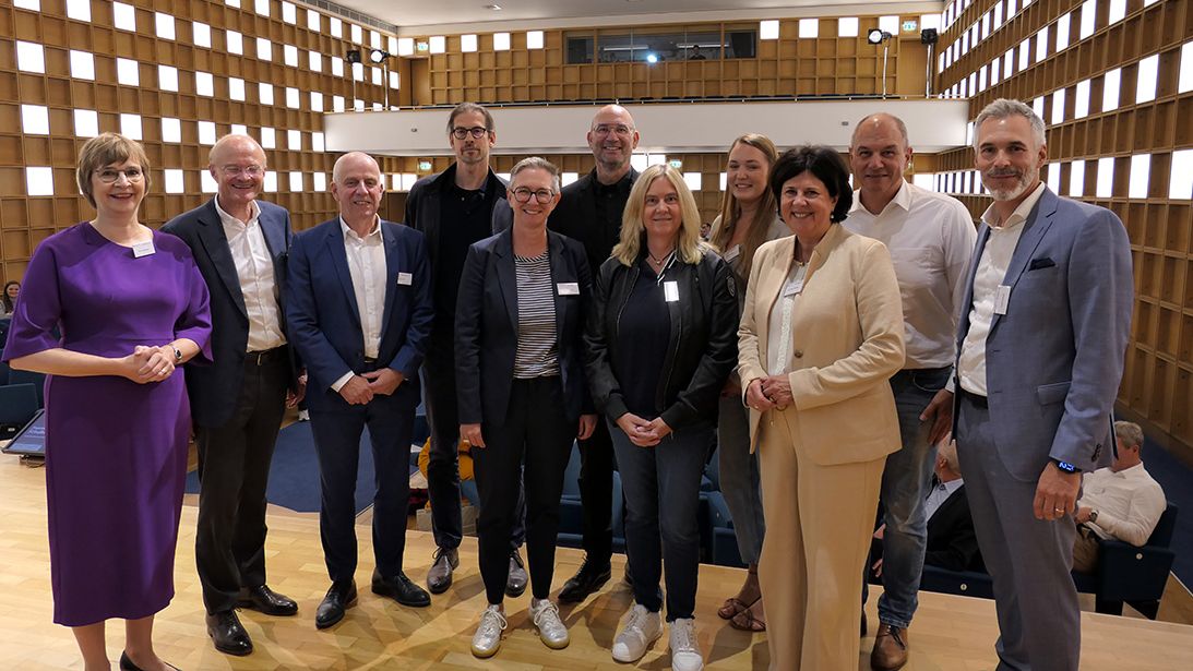 Personen stehen für ein Gruppenbild auf einer Bühne zusammen und lächeln in die Kamera.