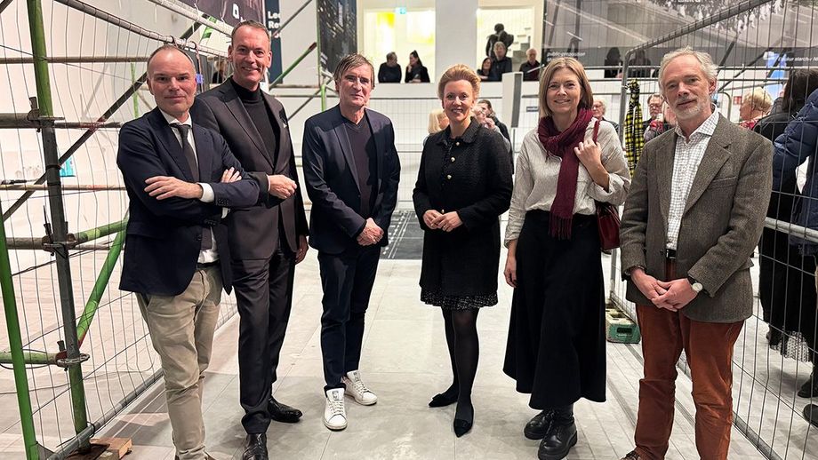 Eine Personengruppe steht beisammen und lächelt in die Kamera. Im Hintergrund unterhalten sich Menschen miteinander.