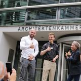 Eine Gruppe junger Leute steht vor einem Gebäude mit der Aufschrift "ARCHITEKTENKAMMER.NRW". Sie werden fotografiert und lächeln und zeigen freundliche Handgesten. - Foto: Ingo Lammert/Architektenkammer NRW