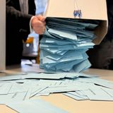 Viele hellblaue Briefumschläge werden aus einer Kiste geschüttet und fallen auf einen Tisch.