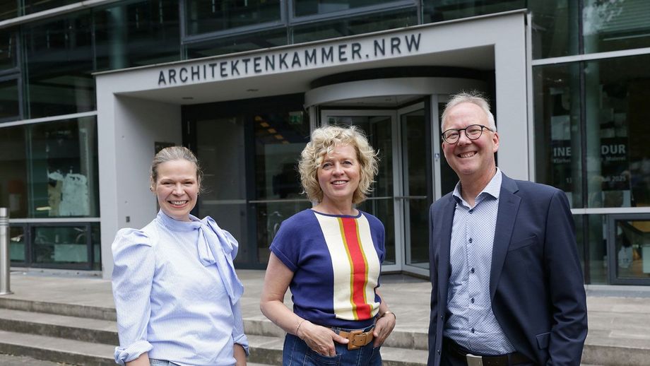 zwei Frauen und ein Mann stehen vor dem Haupteingang der Architektenkammer NRW in einer Reihe.