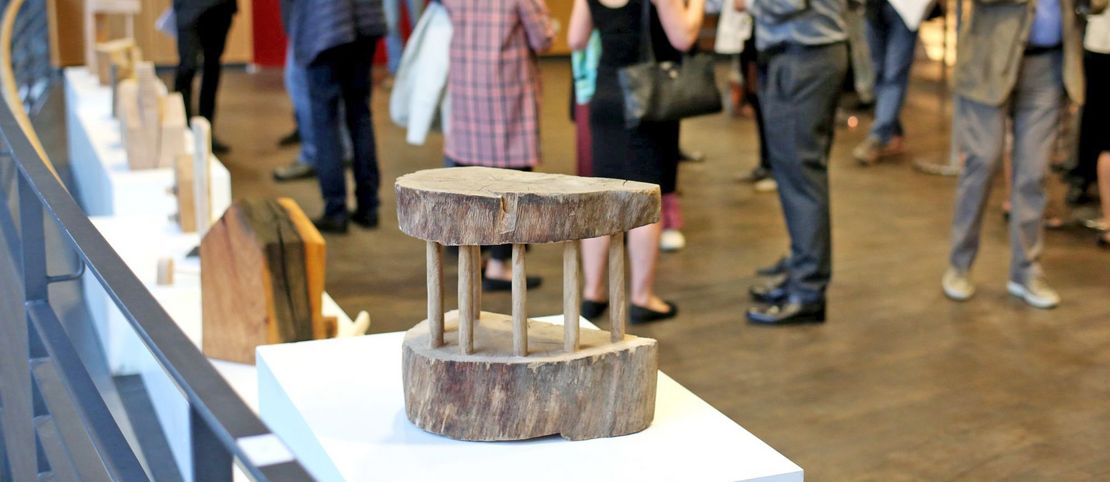Holz-Exponat im Vordergrund mit Ausstellungsbesuchern im Gespräch