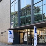 Eine Hausfassade mit großer Fensterfront und kleinen Flaggen vor der Eingangstür.