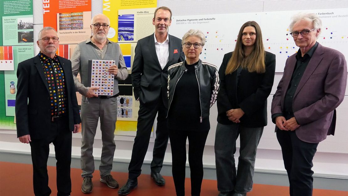 Eine Gruppe von Männern und Frauen steht vor Informationstafeln zum Thema "Farben" und lächelt in die Kamera.