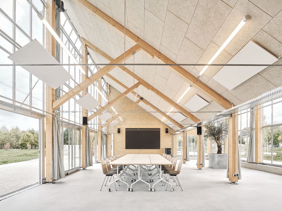 Innenaufnahme des Pavillons mit großen Fensterflächen und einer Holzkonstruktion; Konferenztisch in der Mitte