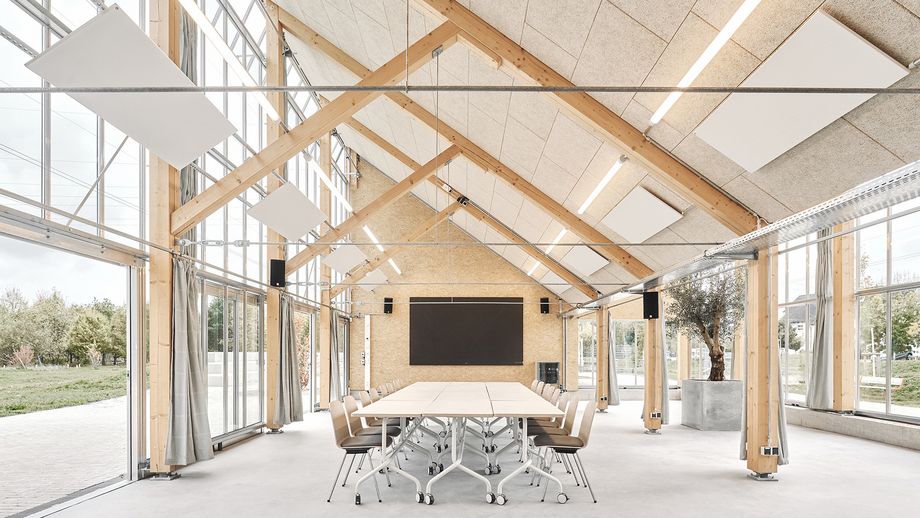 Innenaufnahme des Pavillons mit großen Fensterflächen und einer Holzkonstruktion; Konferenztisch in der Mitte