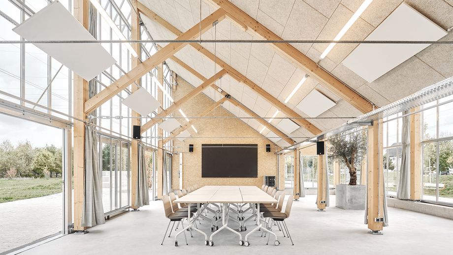 Innenaufnahme des Pavillons mit großen Fensterflächen und einer Holzkonstruktion; Konferenztisch in der Mitte
