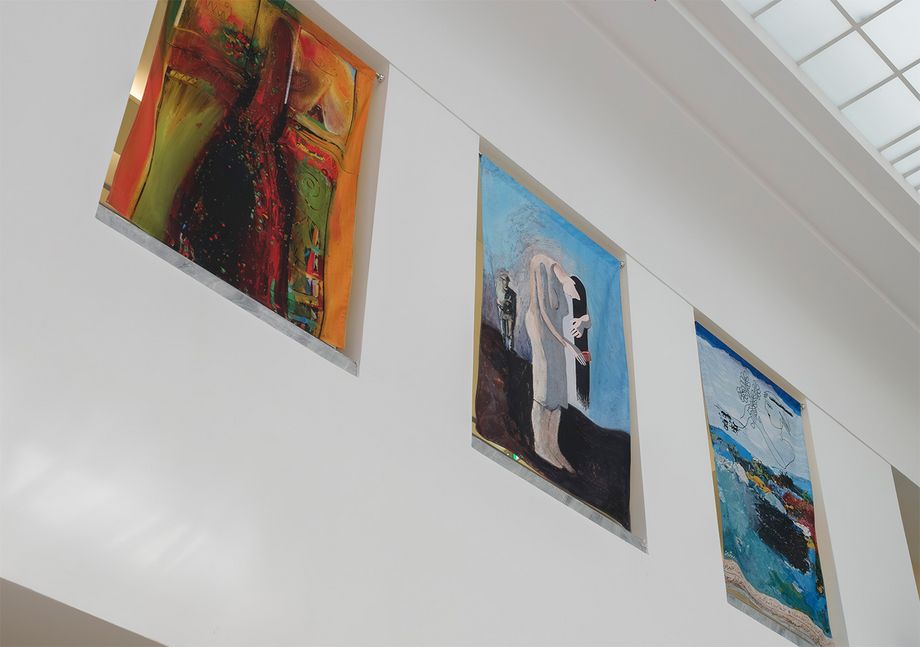 Ein Ausschnitt eines hellen Ausstellungsraums, präsentiert werden an den Wänden bunte Kunstwerke.