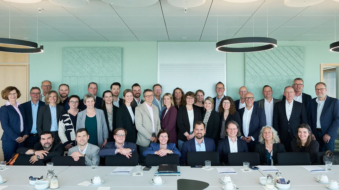 Große Gruppe von Menschen in einem Konferenzraum am Tisch sitzend