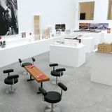 Abgebildet ist die Ausstellung "Werner Ruhnau. Bauen für die offene Gesellschaft" im Baukunstarchiv NRW, die Modelle, Zeichnungen und Fotografie rund um das Werk des Architekten Werner Ruhnau präsentiert. Die Modelle, Fotos, Zeichnungen sind an der Wand und auf Sockeln im Raum verteilt platziert.