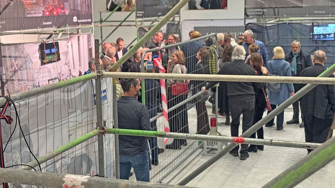 Personen stehen in einem hellen Raum, in dem Bauzäune mit Transparenten hängen.