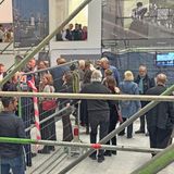 Personen stehen in einem hellen Raum, in dem Bauzäune mit Transparenten hängen.