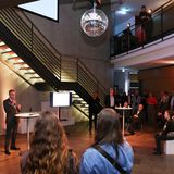 Blick ins Foyer mit Besucher:innen und einem Redner