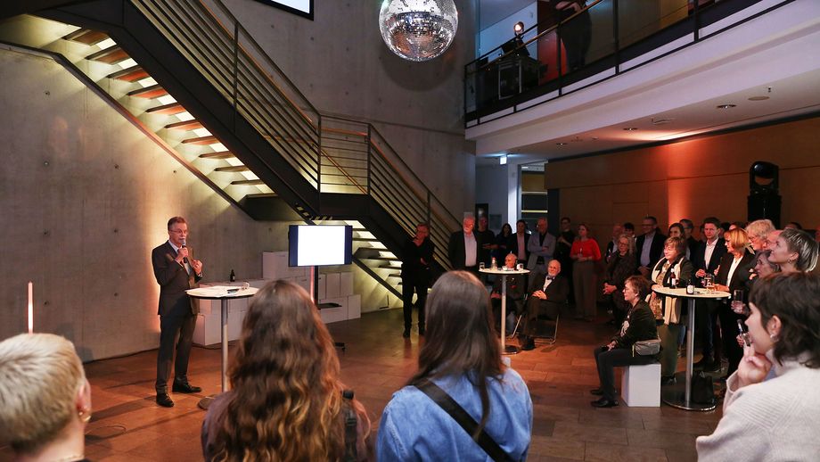 Blick ins Foyer mit Besucher:innen und einem Redner