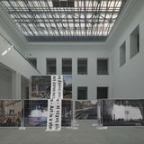 Ein heller Ausstellungsraum, mittig stehen Baugerüste mit Bannern.