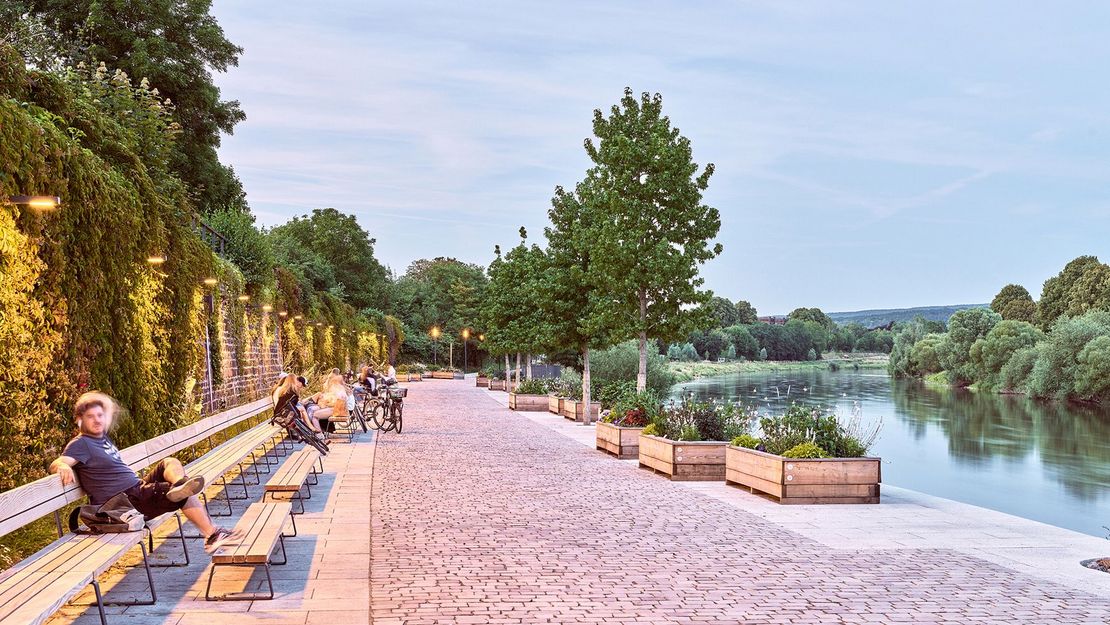 LaGa Höxter 2023 Rendering Flussufer mit von Bänken und Pflanzen umsäumter Uferpromenade mit Menschen auf Bänken sitzend