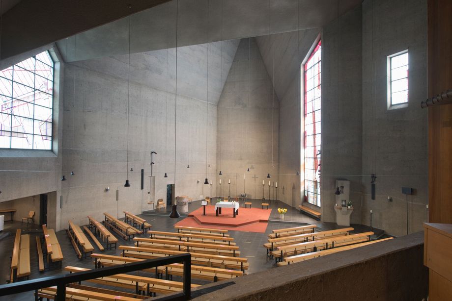 Kircheninnenraum aus Beton mit großen, asymmetrisch angeordneten Fensteröffnungen