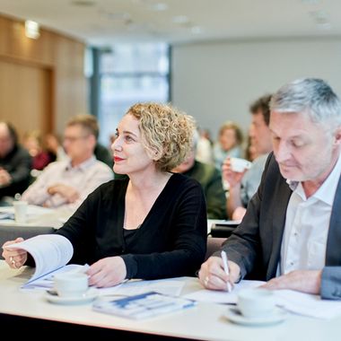 Teilnehmerin und Teilnehmer eines Seminars am Tisch mit Unterlagen