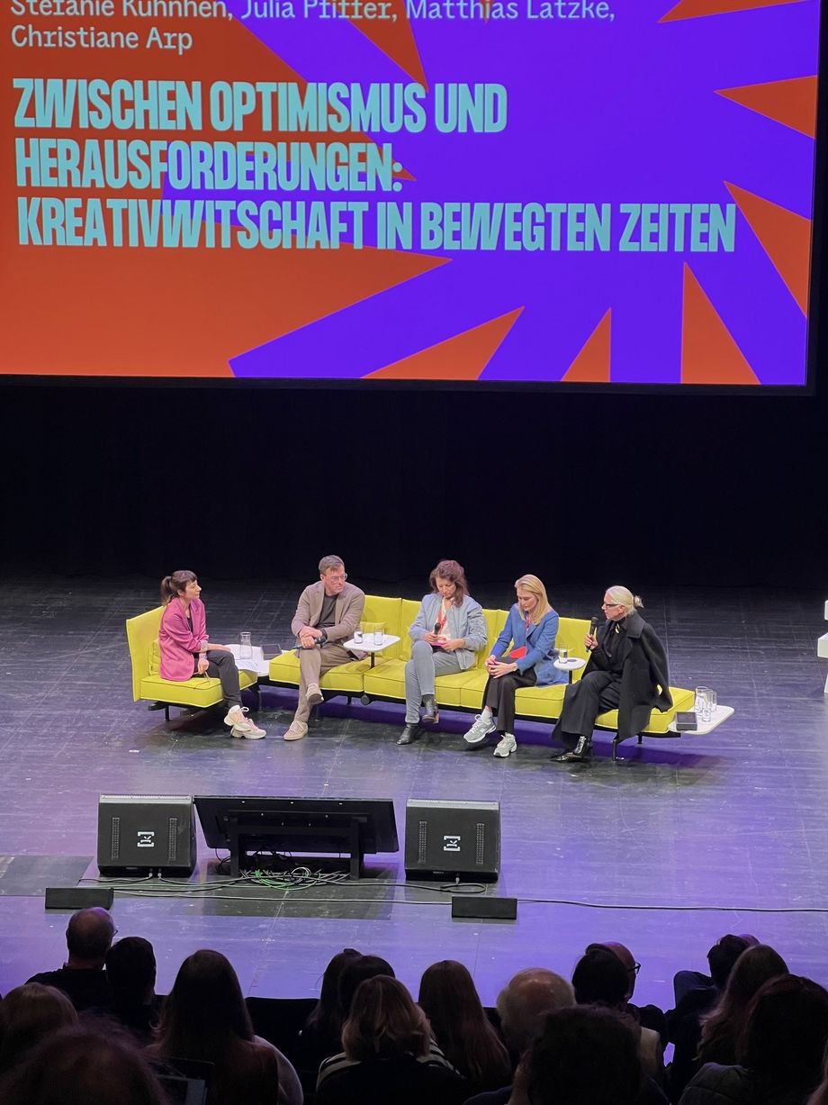 Blick auf Bühne mit fünf Personen, auf gelbem Sofa sitzend