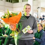 Preisträger mit Blumenstrauß und Gewinnerurkunde vor Publikum der Preisverleihung
