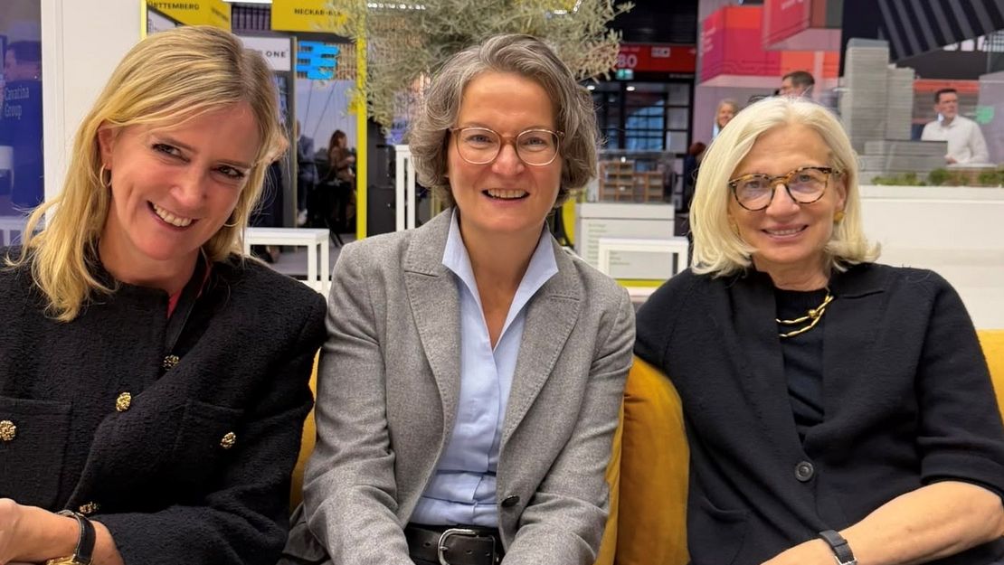 Expo Real-Messe in München 2026. Drei Personen sitzen beisammen und lächeln die Kamera. Im Hintergrund sind Messestände.