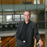 Ein Mann steht in einem offenem Raum und lächelt in die Kamera.