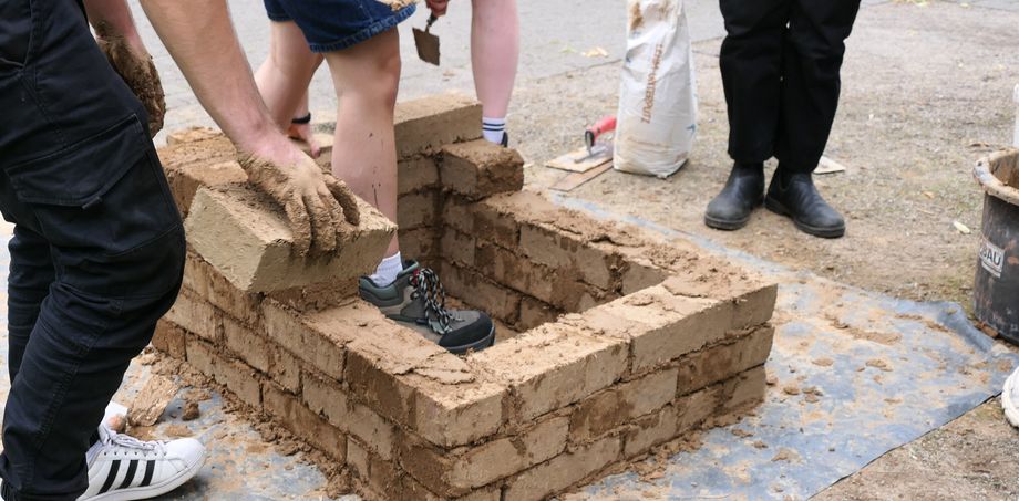 Junge Leute bauen mit Lehmsteinen eine kleine Mauer. - Foto: Architektenkammer NRW