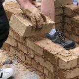 Junge Leute bauen mit Lehmsteinen eine kleine Mauer. - Foto: Architektenkammer NRW