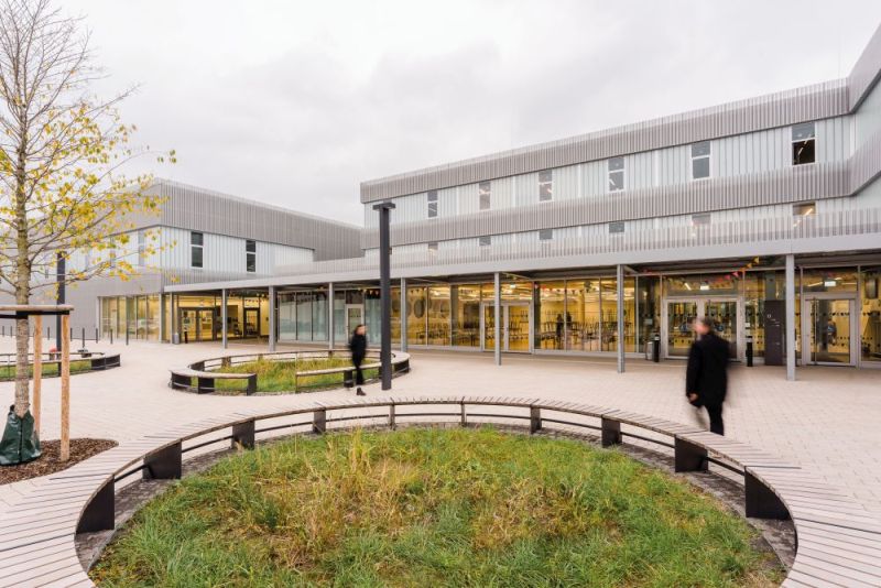 BLick über den Schulhof der Offenen Schule mit grünen Inseln und zwei modernen Gebäuden im Hintergrund