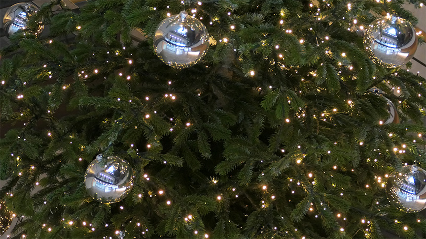 Ausschnitt eines Tannenbaums mit Lichtern und silbernen Weihnachtskugeln.